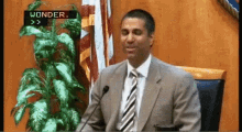 a man in a suit and tie is giving a speech in front of a microphone with wonder written on the screen behind him