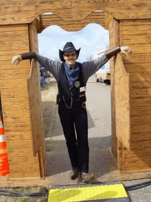 a man in a cowboy outfit is standing in front of a wooden archway