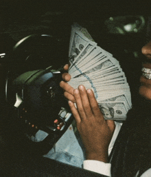 a man in a car holds a stack of 100 dollar bills in his hands