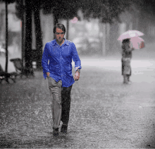 a man in a blue shirt walks through the rain