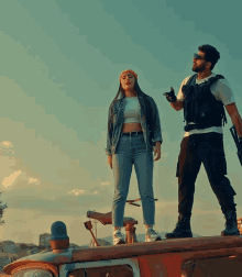 a man and a woman are standing on top of a red car