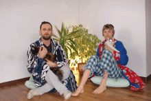 a man and a woman sitting on the floor with their cats