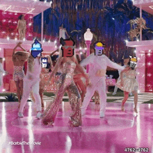 a group of people are dancing on a pink floor with a barbie doll in the background .