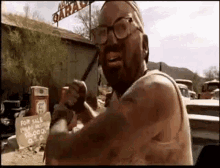 a man with glasses and a beard is holding a hammer in front of a garage for sale sign .