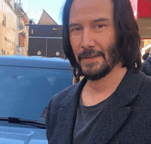 a man with long hair and a beard stands in front of a blue van