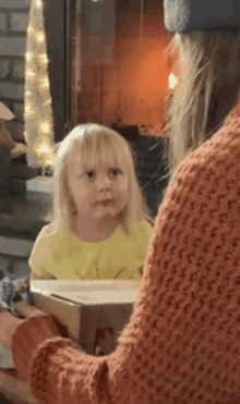 a little girl is sitting in front of a fireplace and looking at a woman .