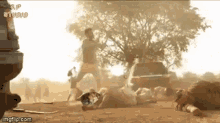 a man is standing next to a car while another man is laying on the ground in the dirt .