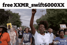 a woman holds her fist in the air in front of a sign that says free xxxmr swift6000xx