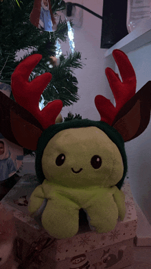 a stuffed animal wearing a reindeer hat is sitting in front of a christmas tree