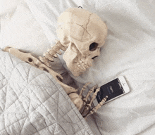 a skeleton is laying on a bed looking at a phone that says alarm