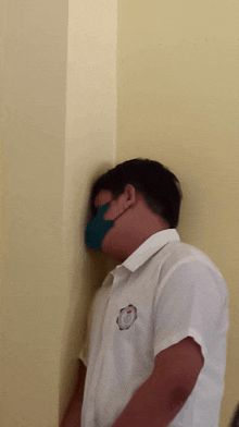 a man wearing a face mask leans against a wall with his head against it