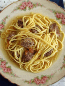 a plate of noodles and meatballs with a floral design