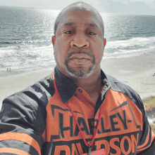 a man wearing a harley davidson shirt stands in front of a beach