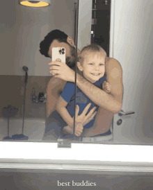 a man is holding a little boy in his arms and taking a selfie in a bathroom mirror