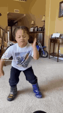 a young boy is dancing in a living room wearing rain boots and a t-shirt with a motorcycle on it .