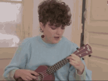 a woman in a blue sweater is playing an ukulele