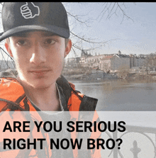 a man wearing a hat and an orange jacket stands in front of a body of water with the words " are you serious right now bro "