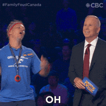 a man in a blue shirt is standing next to a man in a suit holding a family feud binder