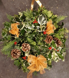 a christmas wreath with pine cones holly berries and a gold bow