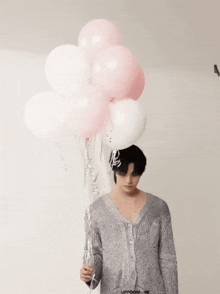 a man in a grey sweater is holding a bunch of balloons