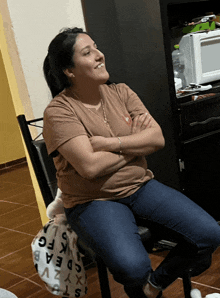 a woman sits in a chair with her arms crossed and a bag with letters on it