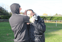 a man with a tattoo on his arm holds another man 's face in a field