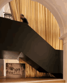 a person is walking down a staircase with a gold curtain behind them