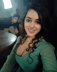 a woman in a green dress takes a selfie with a man in a black shirt behind her