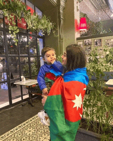 a woman is holding a baby wearing a flag jacket