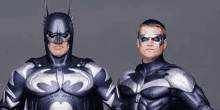 two men in batman and robin costumes are standing next to each other on a gray background .