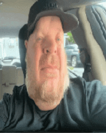 a man with a beard is wearing a hat and taking a selfie in a car .