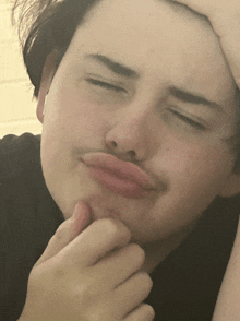 a young man with a mustache is making a funny face with his hand on his chin