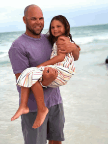 a man in a purple shirt is holding a little girl in his arms