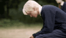 a young man in a blue sweater is kneeling down on the ground with his head down .