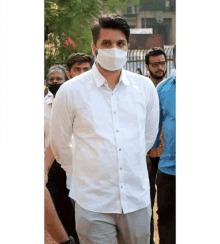 a man wearing a white shirt and a mask is standing in front of a crowd of people .