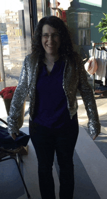 a woman wearing glasses and a sequined jacket smiles