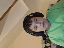 a young boy wearing headphones and a green shirt looks at the camera