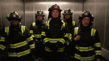 a group of firefighters are standing in an elevator with one wearing a helmet with the letter t on it