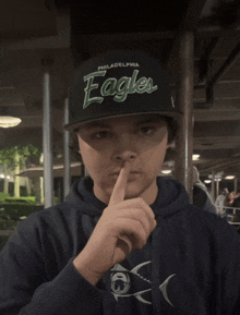 a young man wearing a philadelphia eagles hat holds his finger to his lips