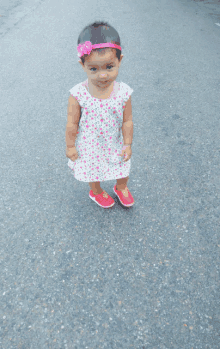 a little girl wearing a pink headband and red shoes is standing on the street