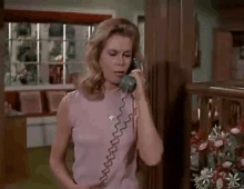 a woman in a pink shirt is talking on a telephone in a living room .