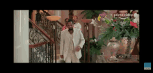 a man in a white suit is walking down a set of stairs in front of a vase of flowers