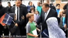 a man in a suit and tie shakes hands with a young boy holding a flag that says ' venstr ' on it