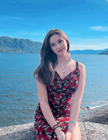 a woman in a red and black dress sits on a rock near the water