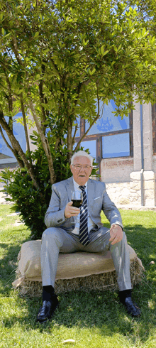 a man in a suit and tie is sitting under a tree with a glass of wine in his hand