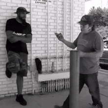 two men are standing in front of a brick wall with a sign on it that says " no parking "