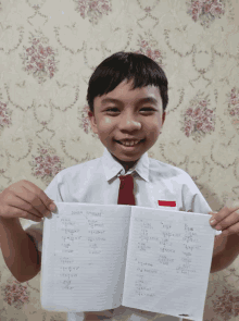 a boy in a white shirt and red tie is holding up a piece of paper with numbers on it