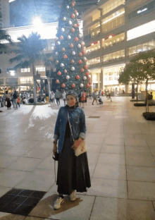 a woman stands in front of a christmas tree