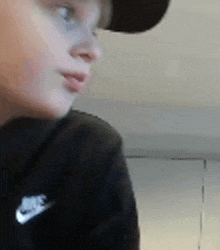 a young boy wearing a hat and a nike shirt is looking at something .