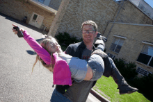 a man is carrying a little girl in his arms and the girl is wearing a pink jacket and a gray shirt